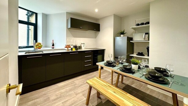A modern kitchen with dark cabinets, a built-in oven, and a dining area with a wooden bench and table set for four. - Massive 3 bedroom - Ground Floor - Near the Beach! (Bournemouth)