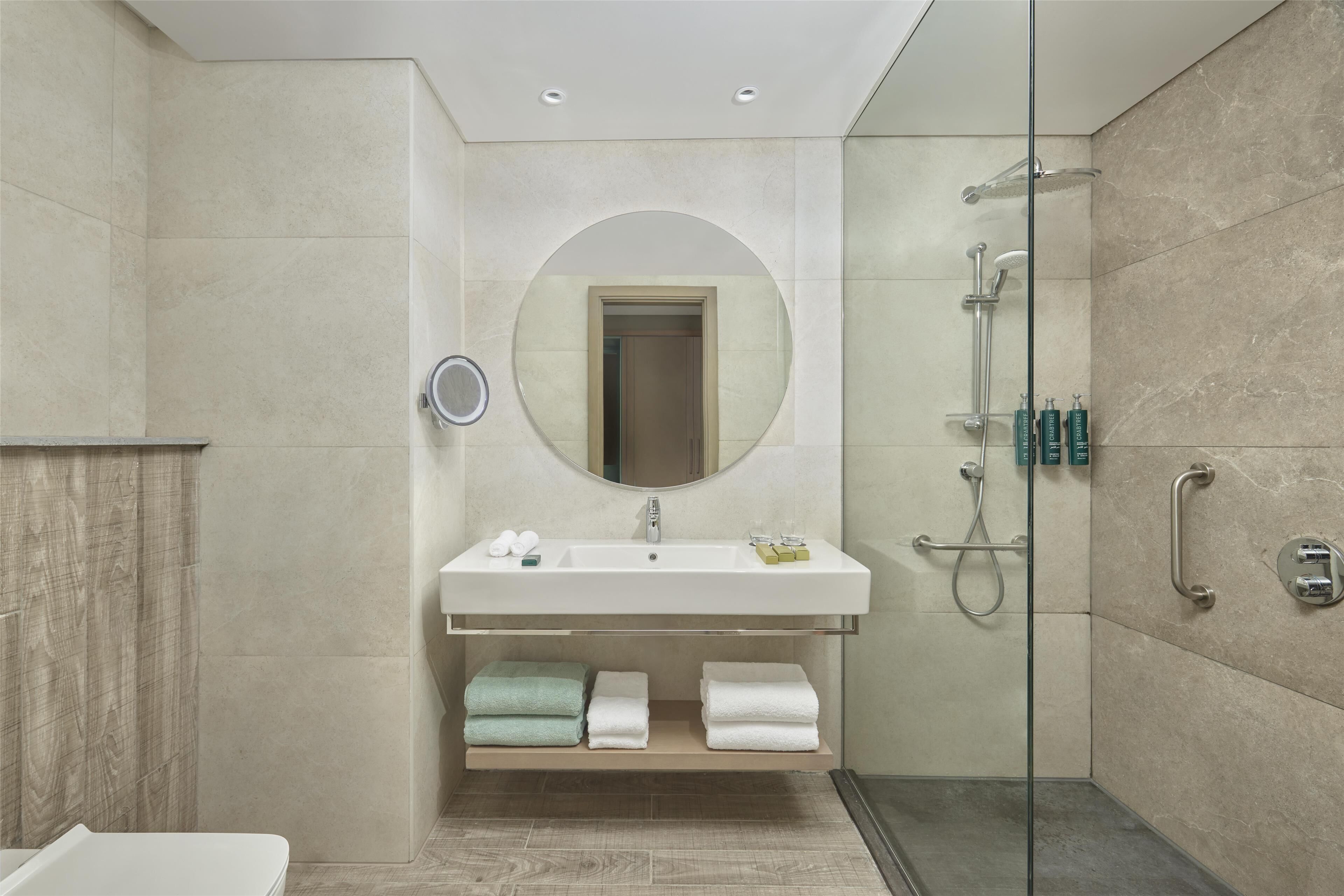 A modern bathroom with a glass-enclosed shower, a vanity with a mirror, and neatly folded towels.