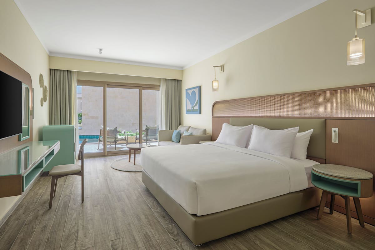 A hotel room with a large bed, a desk, a chair, a small table, and a TV.