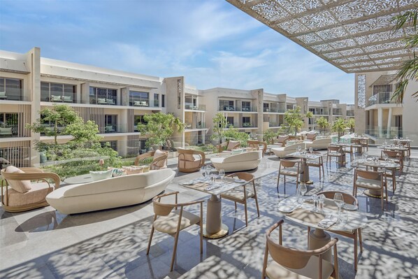 Un espace de restauration extérieur moderne, doté de plusieurs tables et chaises, et entouré d’immeubles avec balcons et de verdure.