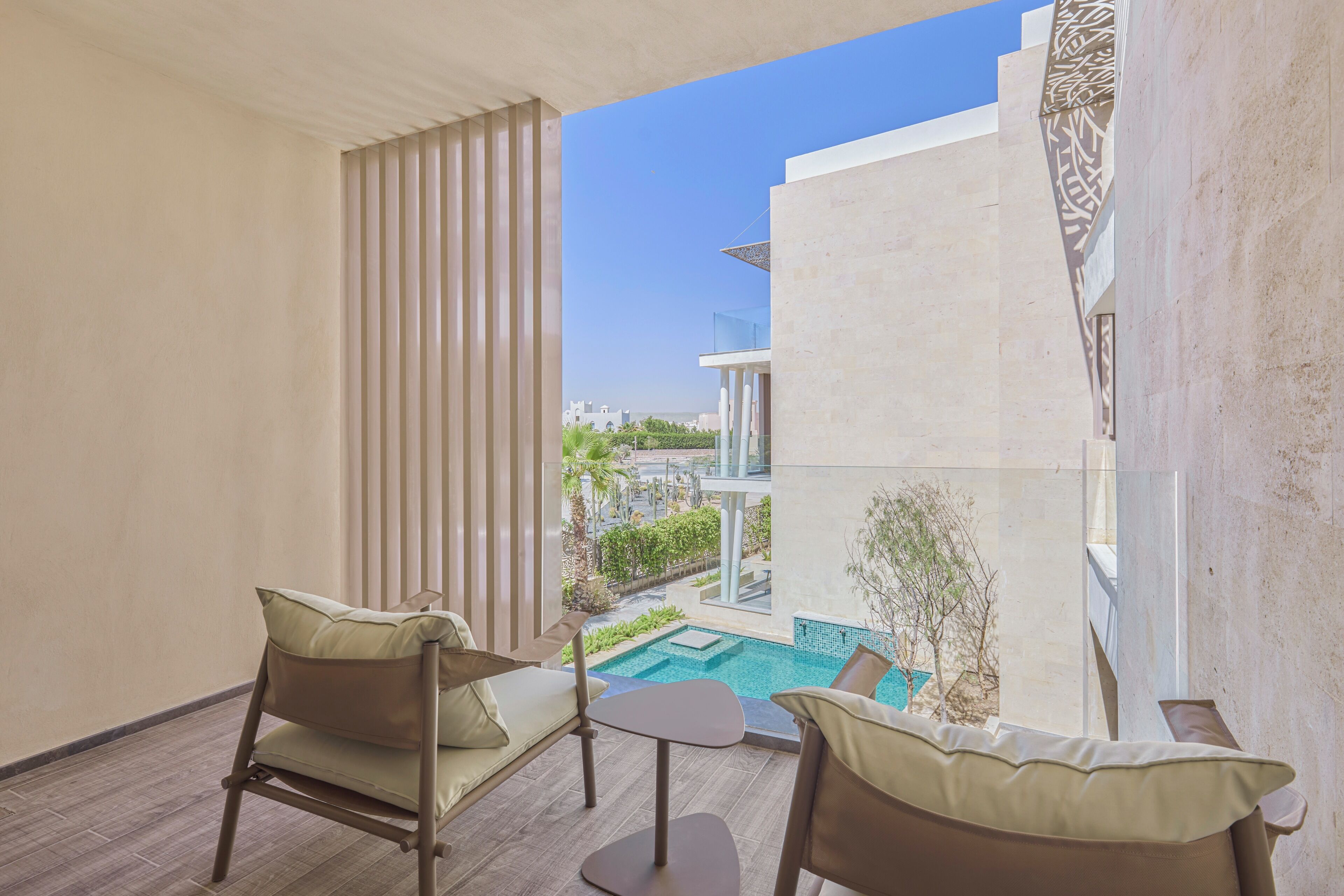 A balcony with two chairs and a small table, overlooking a swimming pool and a building with a modern design.