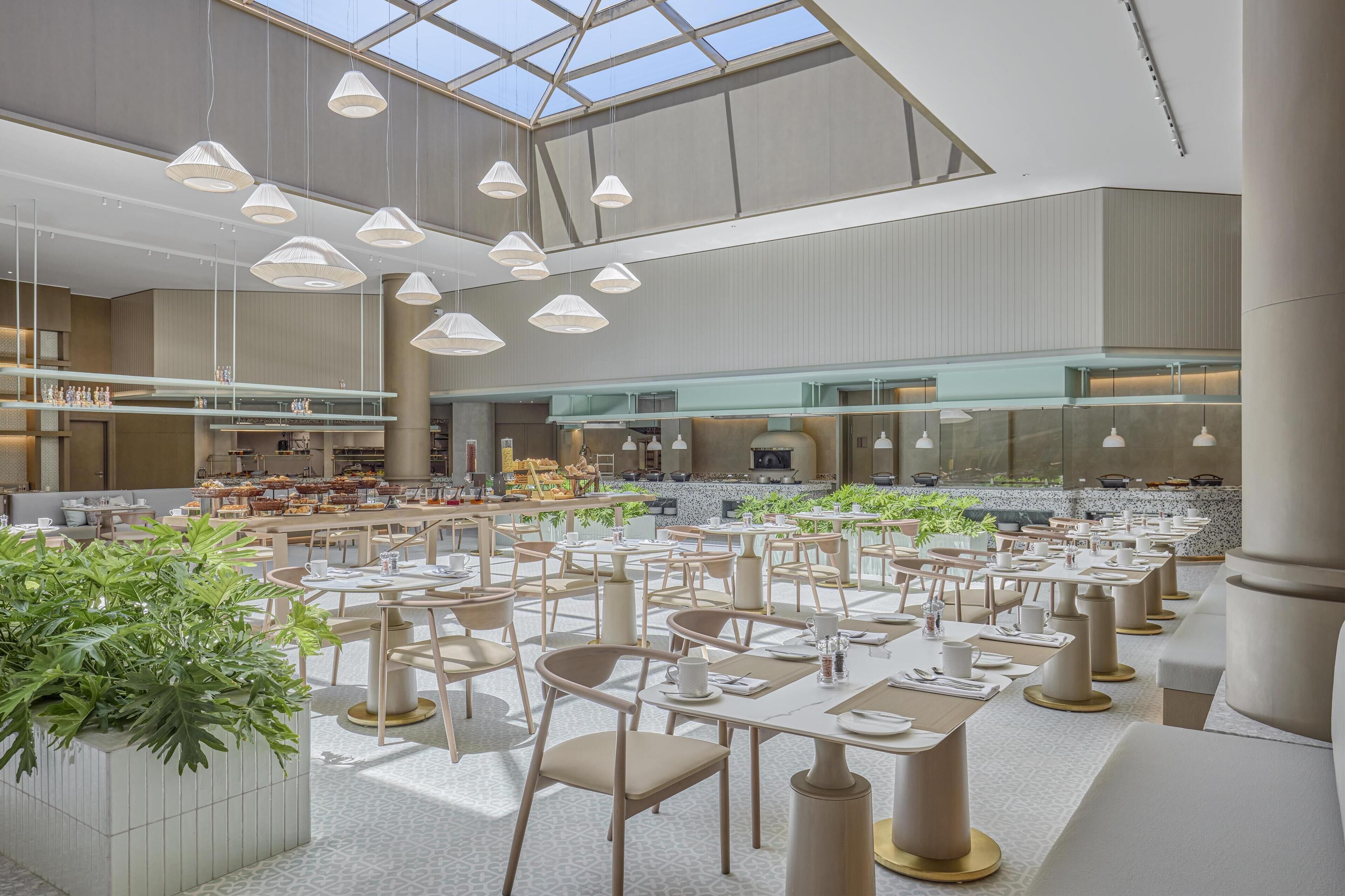 A spacious dining area with multiple tables and chairs, a central kitchen area, and a large skylight.