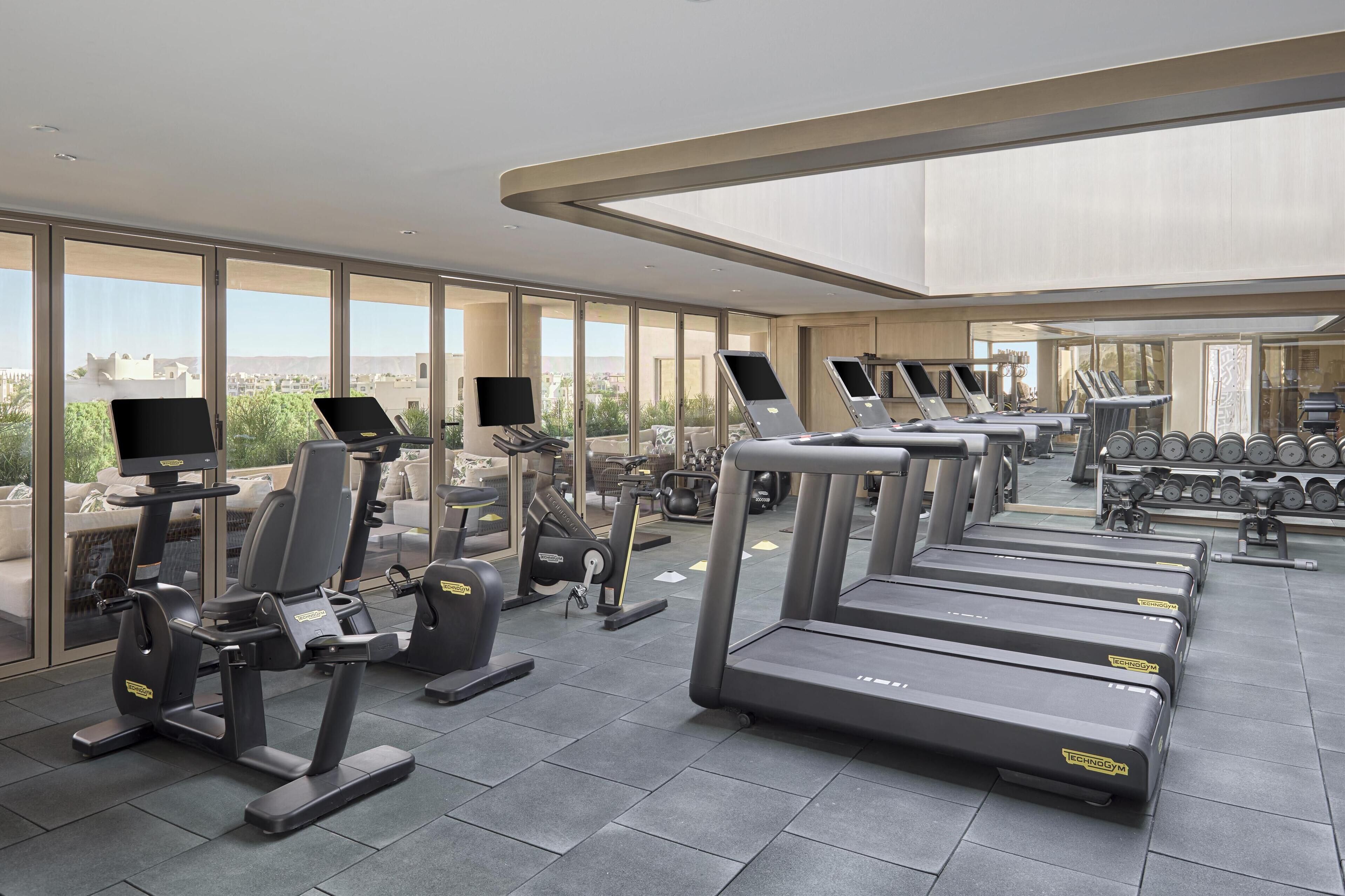 A modern gym with treadmills, elliptical machines, and weight benches.