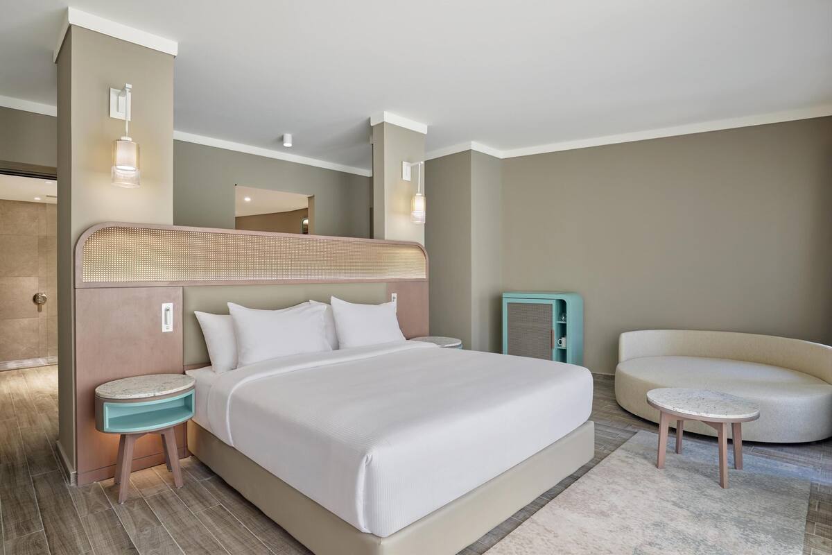 A hotel room with a large bed, a bedside table, a small round table, and a sofa.