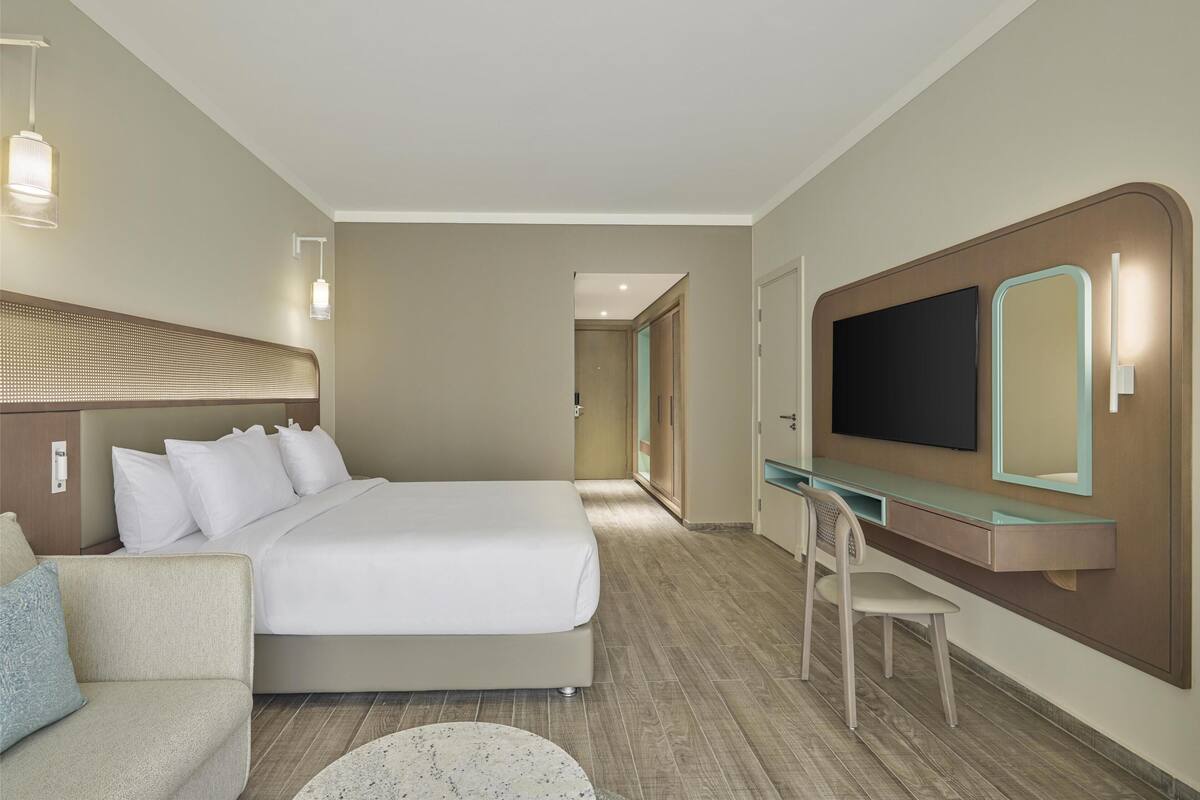 A hotel room with a large bed, a desk with a mirror, a TV, and a chair.