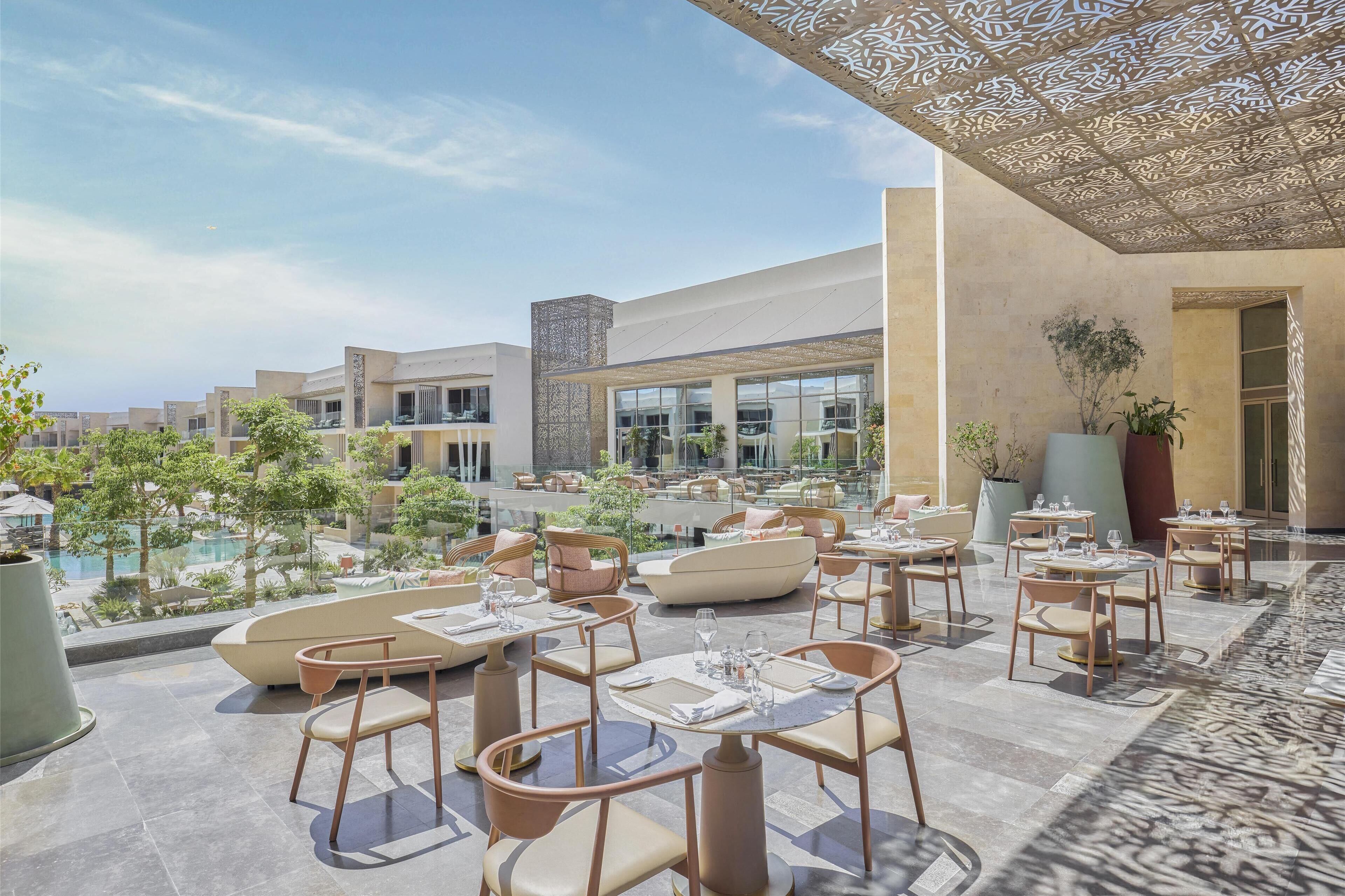 A rooftop dining area with outdoor seating, a pool, and a view of other buildings.