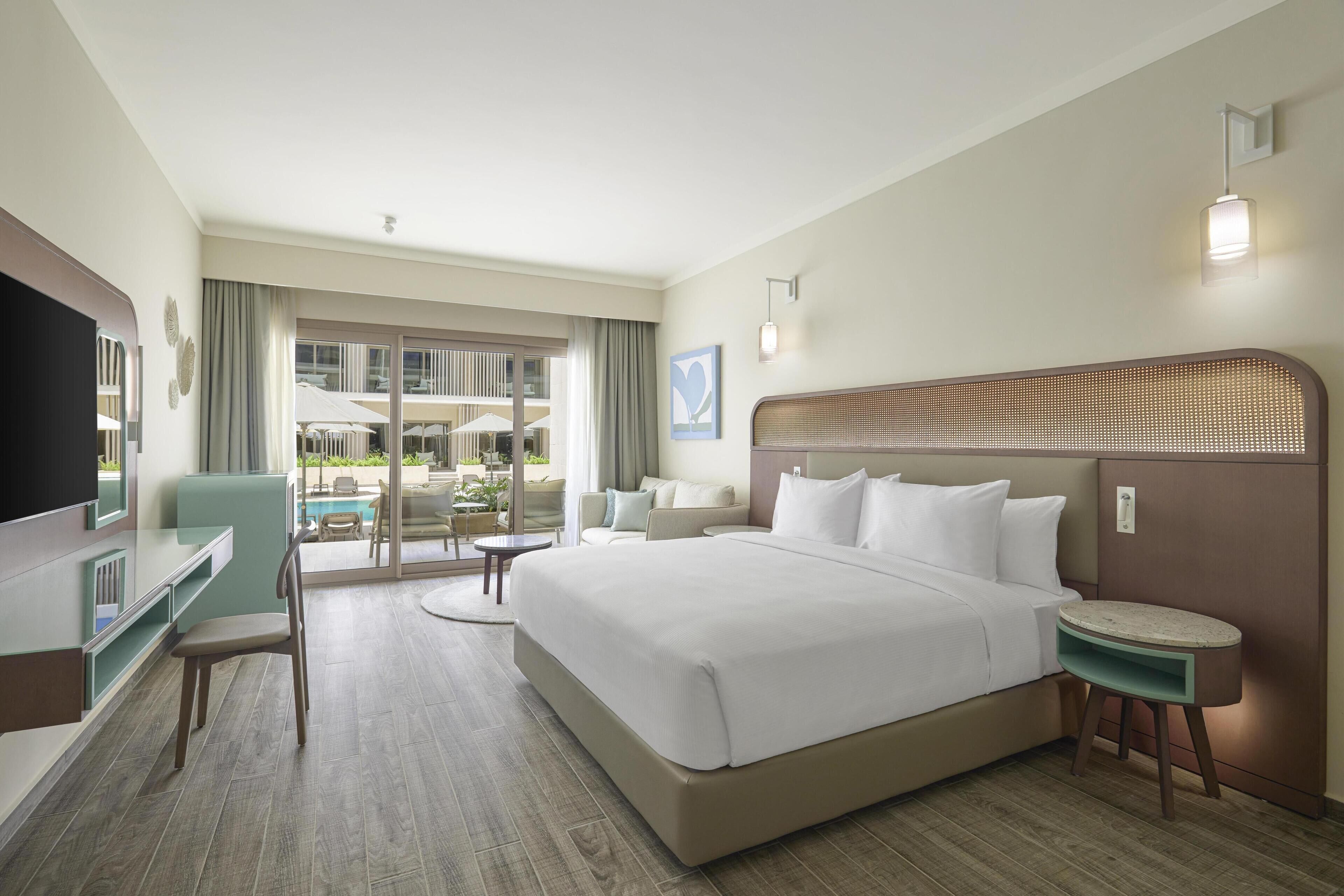 Hotelkamer met een groot bed, bureau, stoel, klein tafeltje en uitzicht op het buitengebied.