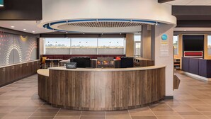 A modern reception area with a curved wooden counter, a large window offering a view, and a seating area with a red couch. - Tru By Hilton Lodi (Lodi)
