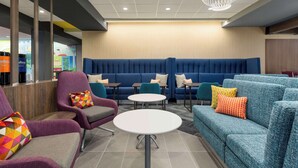 A modern lounge area with blue seating, round tables, and colorful pillows. - Tru By Hilton Lodi (Lodi)