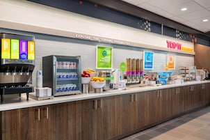 Un moderno espacio para comidas con dispensador de zumo, estación de yogur y avena, y una variedad de alimentos.
