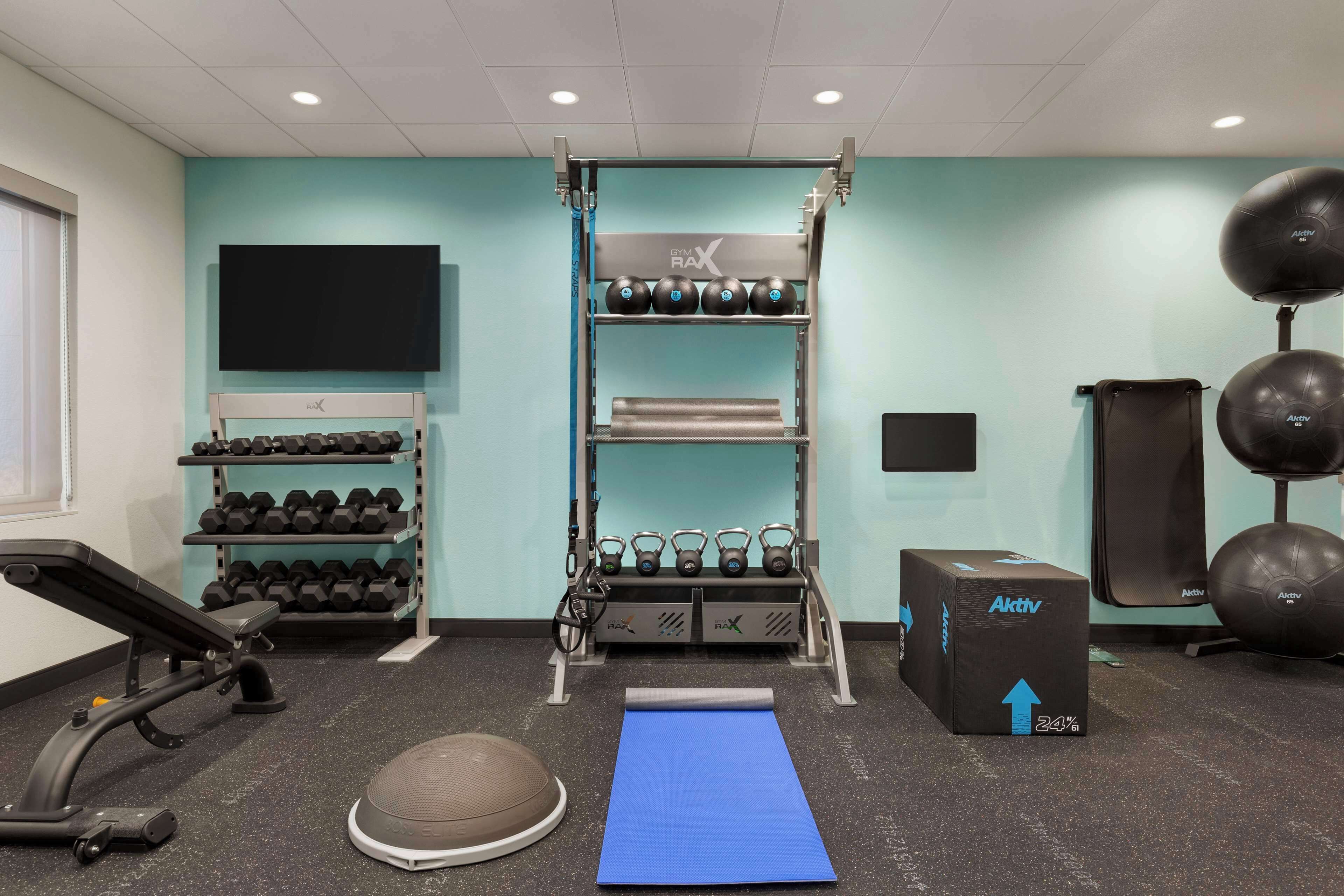 A gym with a pull-up bar, dumbbells, kettlebells, a stationary bike, a yoga mat, and a box labeled "Aktiv".