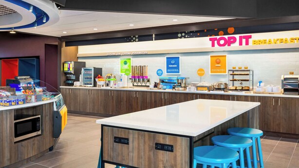 A modern breakfast area with a counter, stools, and various food items. - Tru By Hilton Lodi (Lodi)