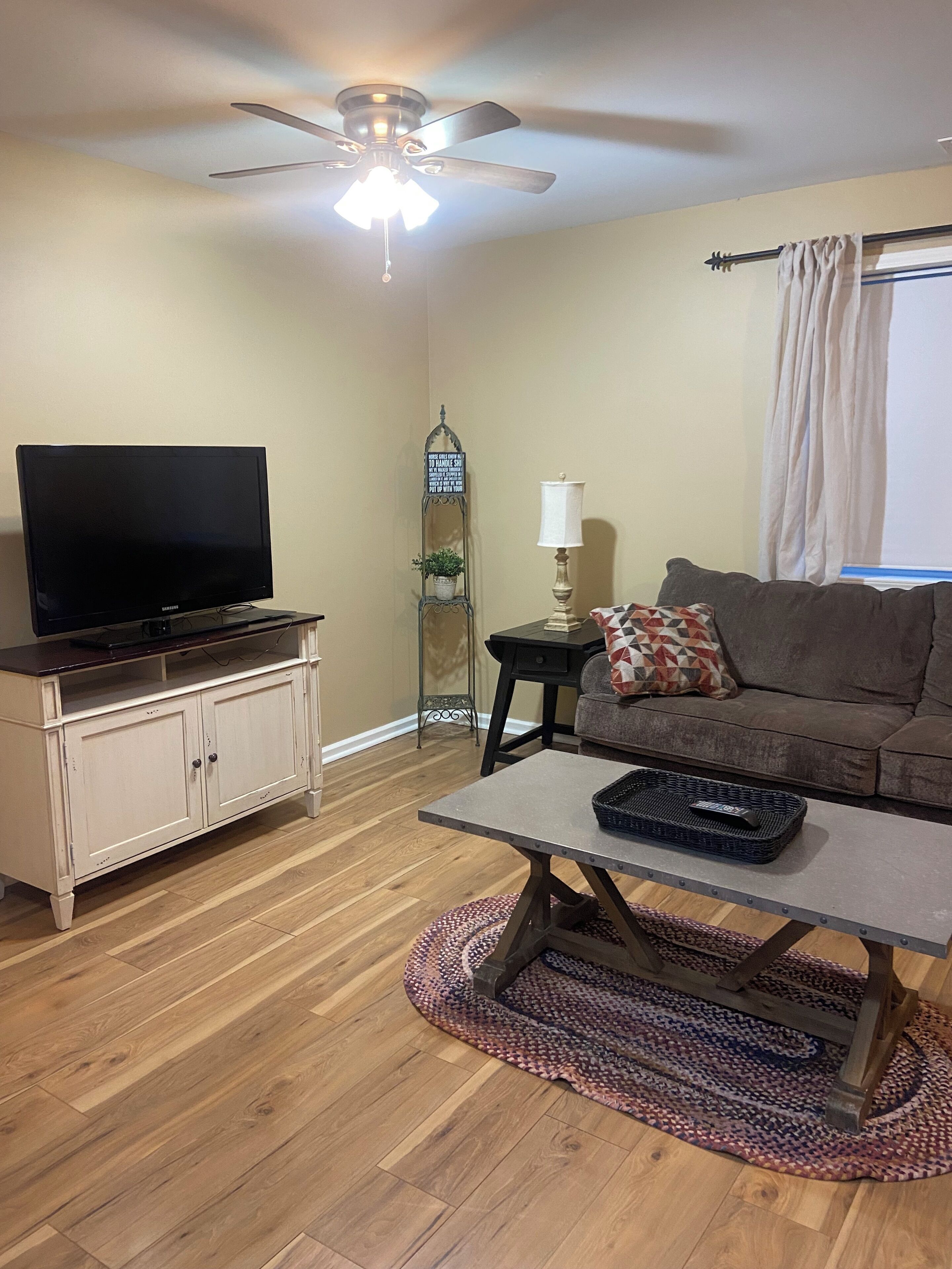 A living room with a television on a cabinet, a ceiling fan, a sofa, a coffee table, and a patterned rug.