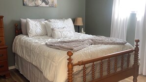 A bedroom with a wooden bed, a red rug, a painting on the wall, and a window with curtains.
