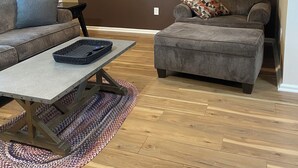A living room with a brown accent wall, a gray sofa, a gray ottoman, a coffee table, and a lamp.