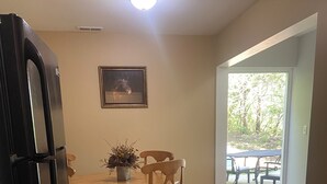 A dining area with a wooden table and chairs, a potted plant, and a framed picture on the wall.