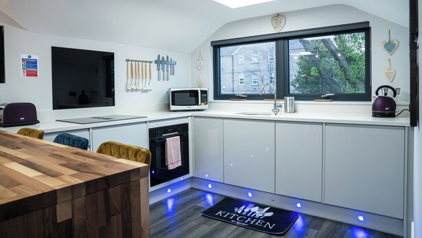 A modern kitchen with white cabinets, a built-in microwave, a kettle, and a window overlooking a tree. - Annex, 2 Bed, Sleeps 4, Parking (Ossett)