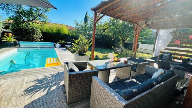 Un patio trasero con piscina, mobiliario exterior y una pérgola.