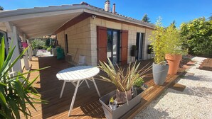 Un patio cubierto con piso de madera, una mesa blanca y plantas en macetas.