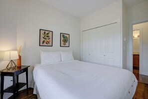 A bedroom with a large bed, a nightstand with a lamp, and two framed botanical prints on the wall. - Corner Unit w Large Deck & Amazing View (West Kelowna)