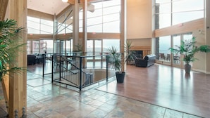 A spacious lobby with a central staircase, large windows, and indoor plants. - Corner Unit w Large Deck & Amazing View (West Kelowna)