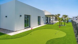 A modern building with a flat roof, large glass doors, and a well-maintained lawn with a putting green. - Villa Tirma by Villa Plus (Playa Blanca)