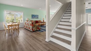 A spacious living room with hardwood floors, a dining area with wooden chairs, a colorful sofa, and a staircase. - Indulge in the epitome of coastal living with Celtic Dream-pool (North Myrtle Beach)