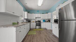 A modern kitchen with white cabinets, stainless steel appliances, and a blue accent wall. - Indulge in the epitome of coastal living with Celtic Dream-pool (North Myrtle Beach)