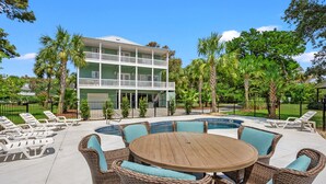A pool area with a round wooden table and wicker chairs, surrounded by lounge chairs. - Indulge in the epitome of coastal living with Celtic Dream-pool (North Myrtle Beach)