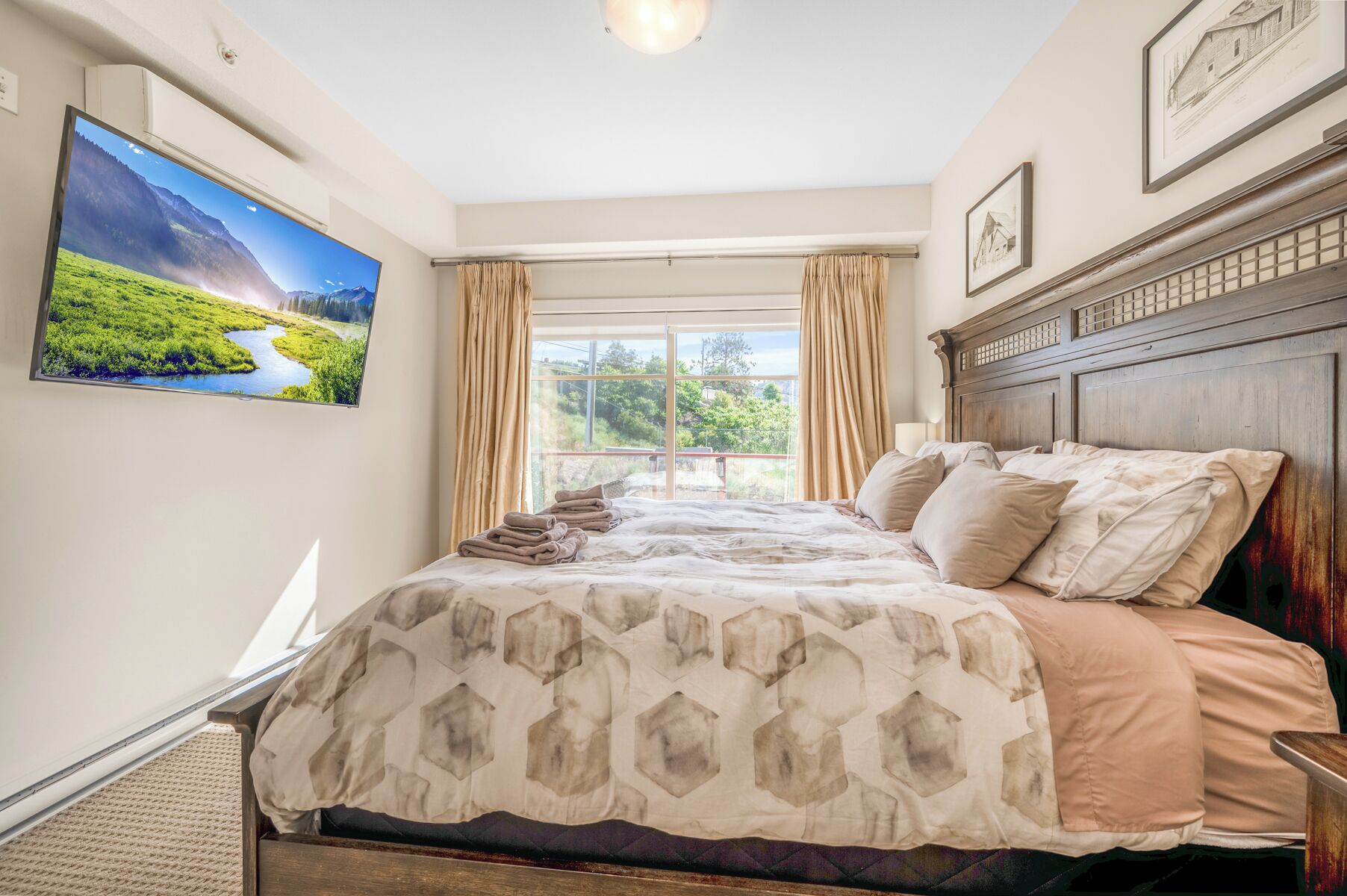 Ein Schlafzimmer mit einem großen Bett, einem Fernseher an der Wand und Blick auf Grünflächen.