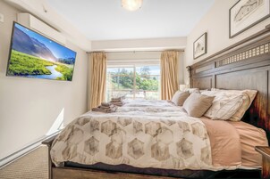 Un dormitorio con una cama grande, un televisor en la pared y vistas al exterior con vegetación.