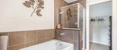 A modern bathroom with a bathtub, a glass shower enclosure, and a decorative leaf wall art piece.