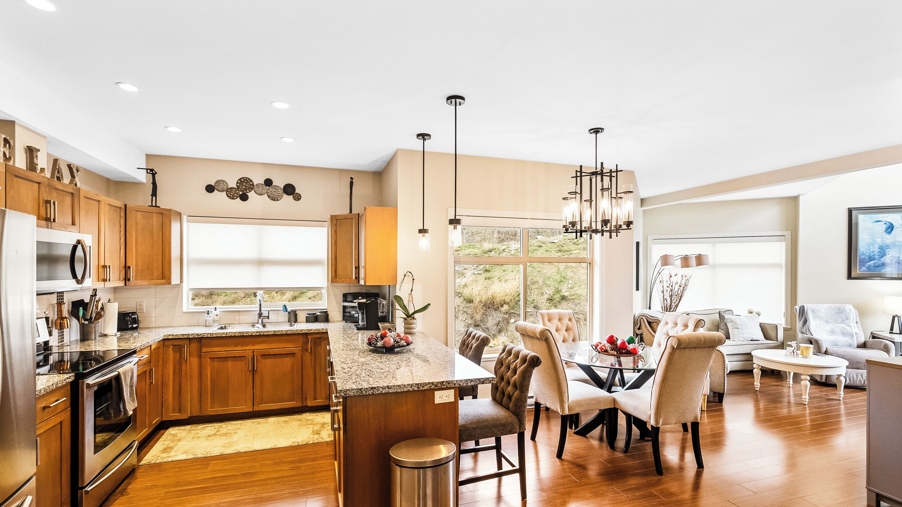 Una cocina moderna con armarios de madera, encimera de granito y comedor con candelabro.