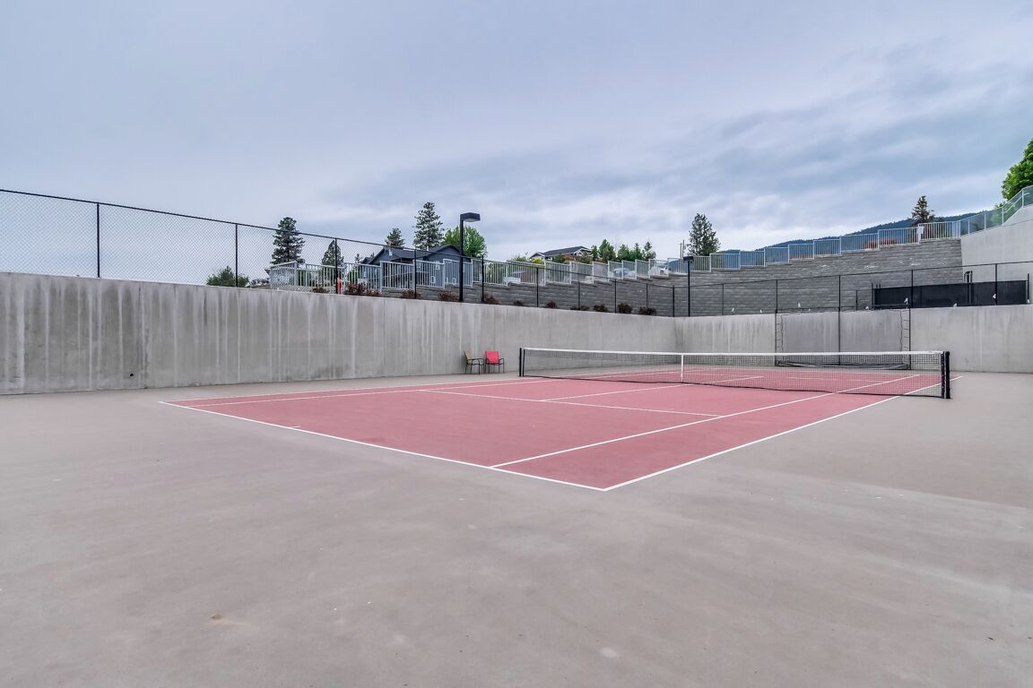 Una cancha de tenis al aire libre con red, rodeada por un muro de hormigón y una valla.