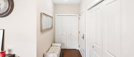 A hallway with a bench, a framed mirror, and a door with a light switch.