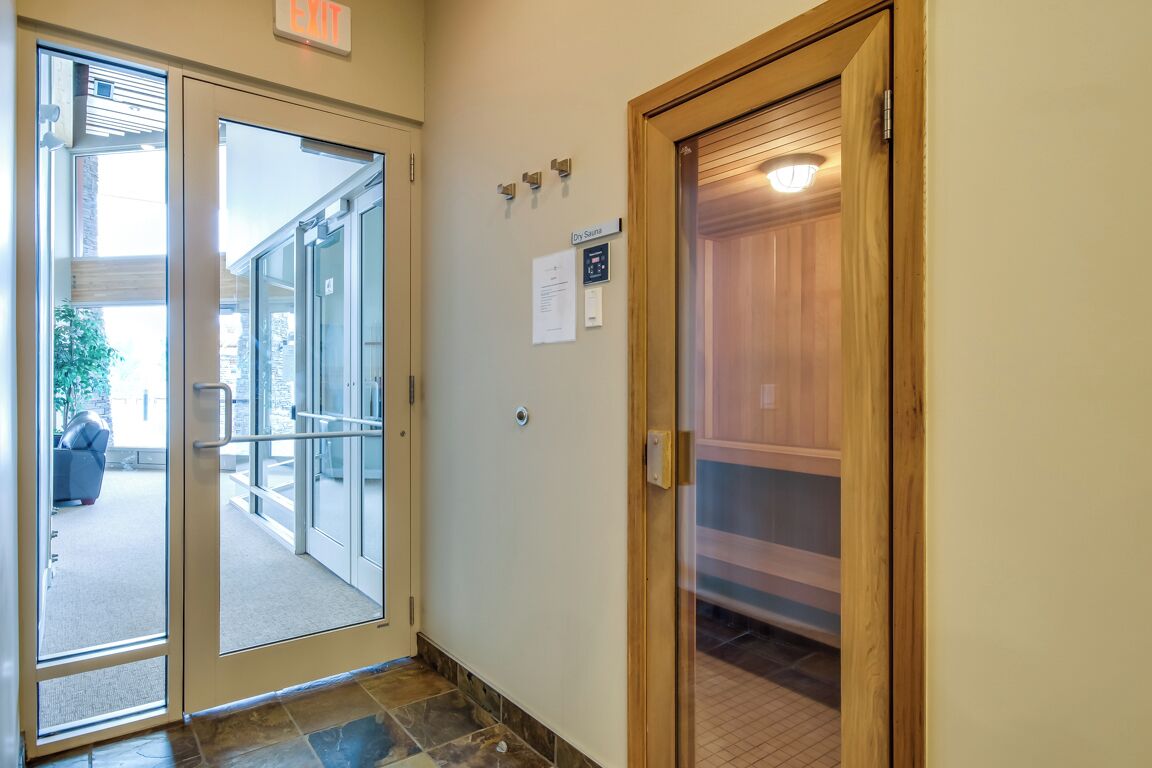 Entrada de un hotel con puerta de vidrio, señal de salida y puerta de madera que conduce a una sauna.