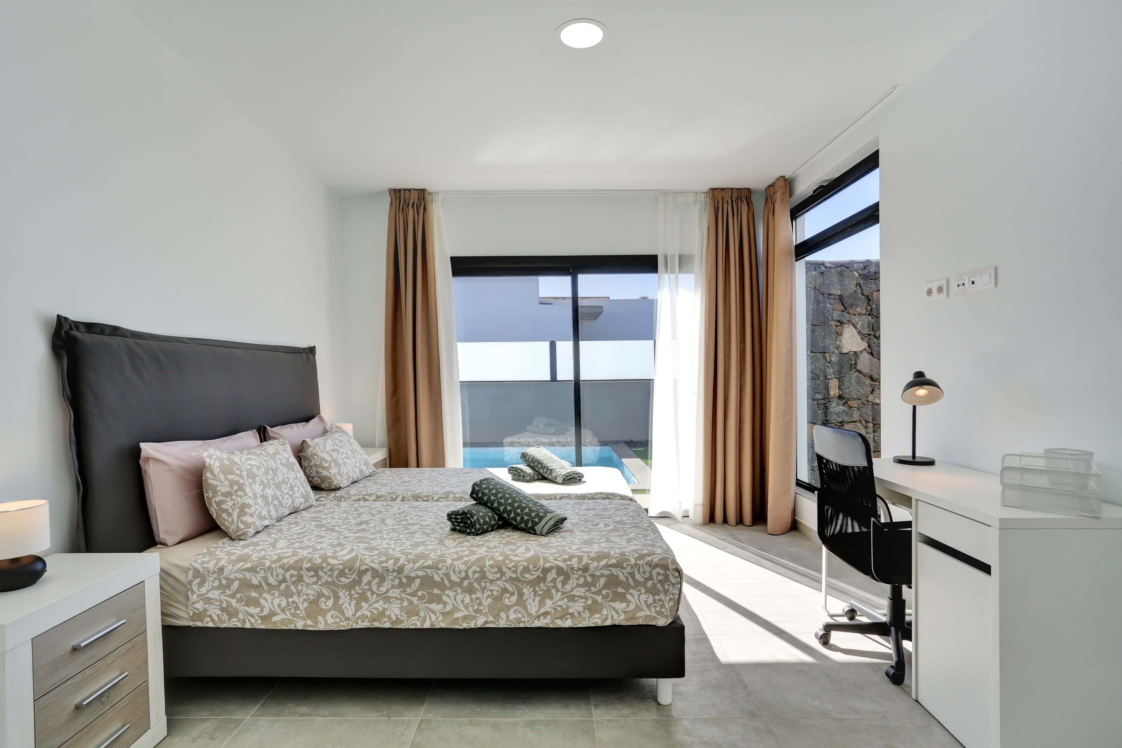 Une chambre moderne avec un grand lit, un bureau et une vue sur une piscine.