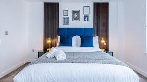 A hotel room with a large bed, a blue headboard, and framed pictures on the wall.