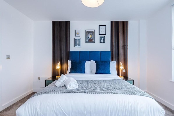 A hotel room with a large bed, a blue headboard, and framed pictures on the wall. - Cosy 2 bed Apt n/ City Centre & Mediacity (Salford)