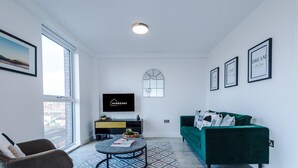 A modern living room with a sofa, a coffee table, and a TV. There is a window, a wall-mounted TV, and framed pictures.