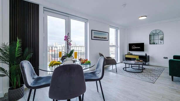A modern living room with a dining area, large windows, a flat-screen TV, and a city view.