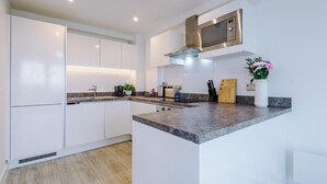 A modern kitchen with white cabinetry, a granite countertop, a stainless steel microwave, and a small island with a sink.