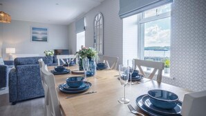 Comedor con una mesa de madera dispuesta para cuatro, vajilla azul y sillas blancas.