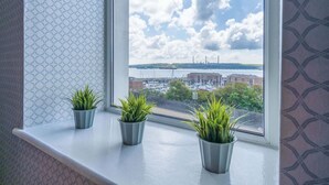 Una ventana con tres plantas en macetas en un alféizar, con vista a un puerto deportivo con barcos y edificios.