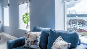 A blue sofa with nautical-themed cushions in a room with large windows overlooking a marina.