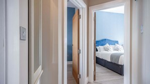 A hallway leading to a bedroom with a blue headboard and white bedding.