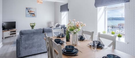 A modern living room with a sofa, dining table set for four, and a TV.
