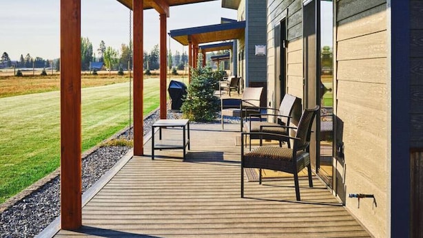 A covered outdoor deck with wooden flooring and seating, overlooking a grassy field.