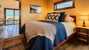 A bedroom with a large bed, a window, a painting, and a view of the outdoors.