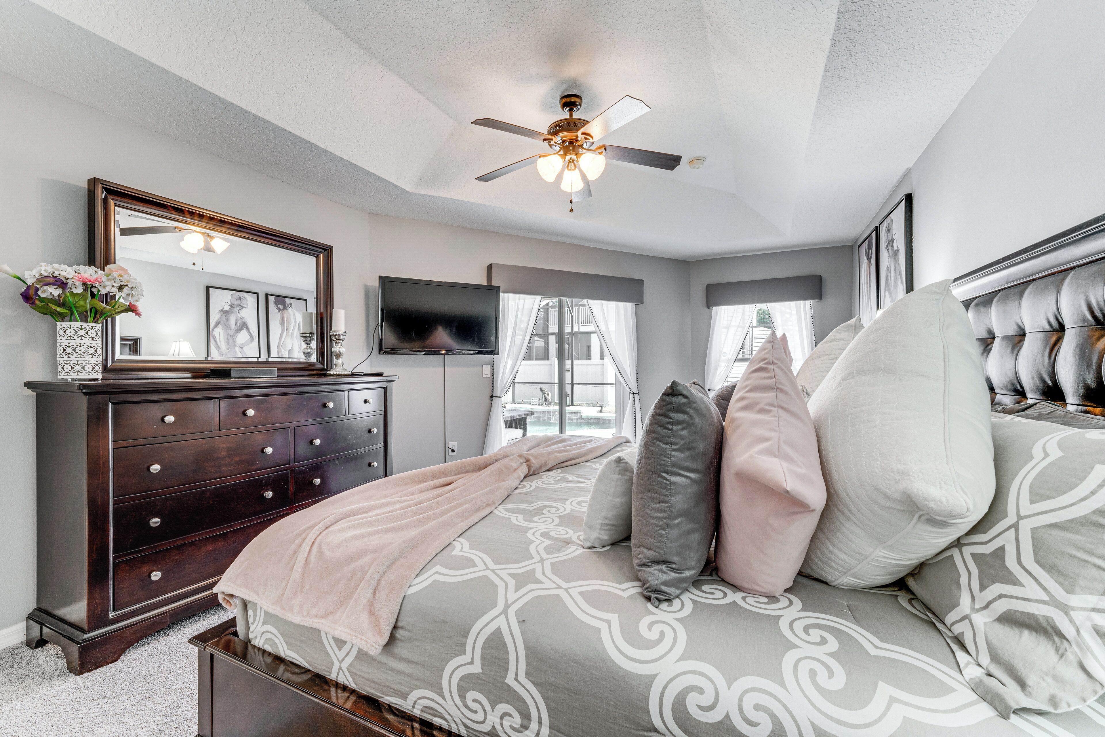 A bedroom with a bed, dresser, television, and a ceiling fan.